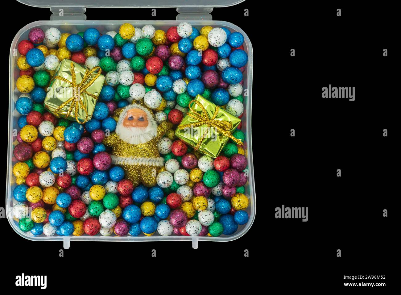 Père Noël avec pile de petites boules de thermocol colorées et boîte cadeau dans une boîte en plastique isolée sur fond noir. vue de dessus Banque D'Images