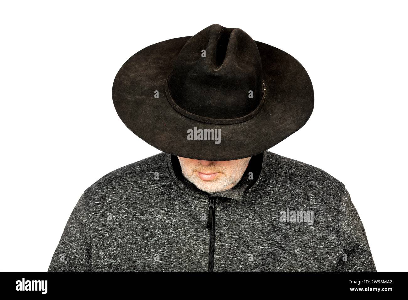Homme caucasien sérieux d'âge moyen dans le chapeau de cow-boy noir sale regardant vers le bas sur fond blanc Banque D'Images