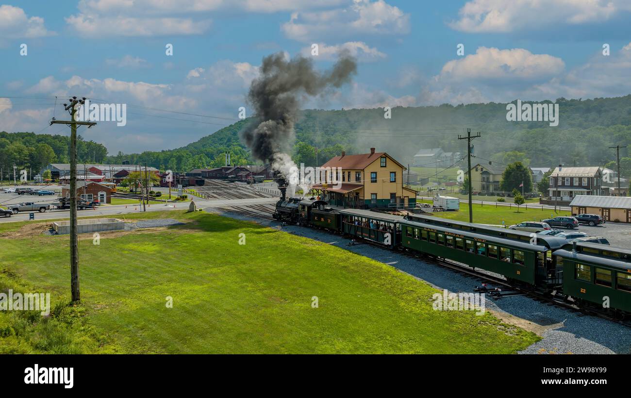 Une vue aérienne d'un train de passagers à vapeur à voie étroite, arrivant dans la gare, soufflant de la fumée, par une journée d'été ensoleillée Banque D'Images