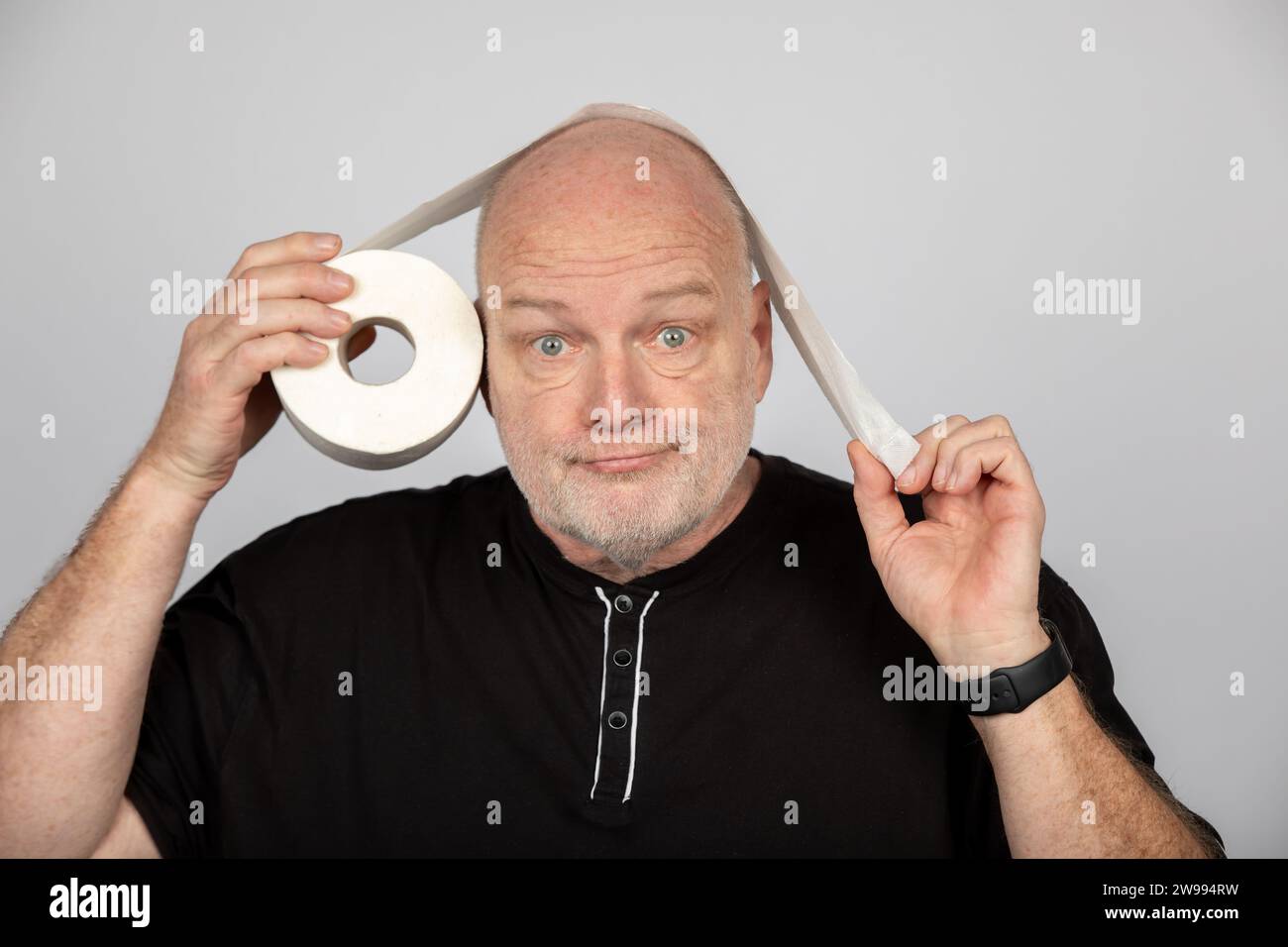 Homme d'âge moyen avec rouleau de papier toilette comme sur ou sous concept sur fond gris Banque D'Images