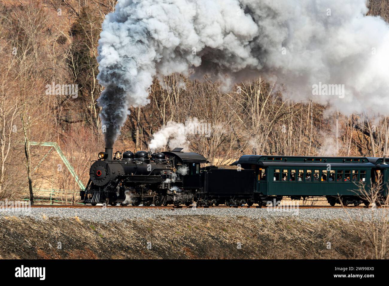 Vue d'un train de passagers à vapeur restauré à voie étroite, soufflant de la fumée noire et de la vapeur blanche, voyageant à travers les terres agricoles par un jour d'hiver Banque D'Images