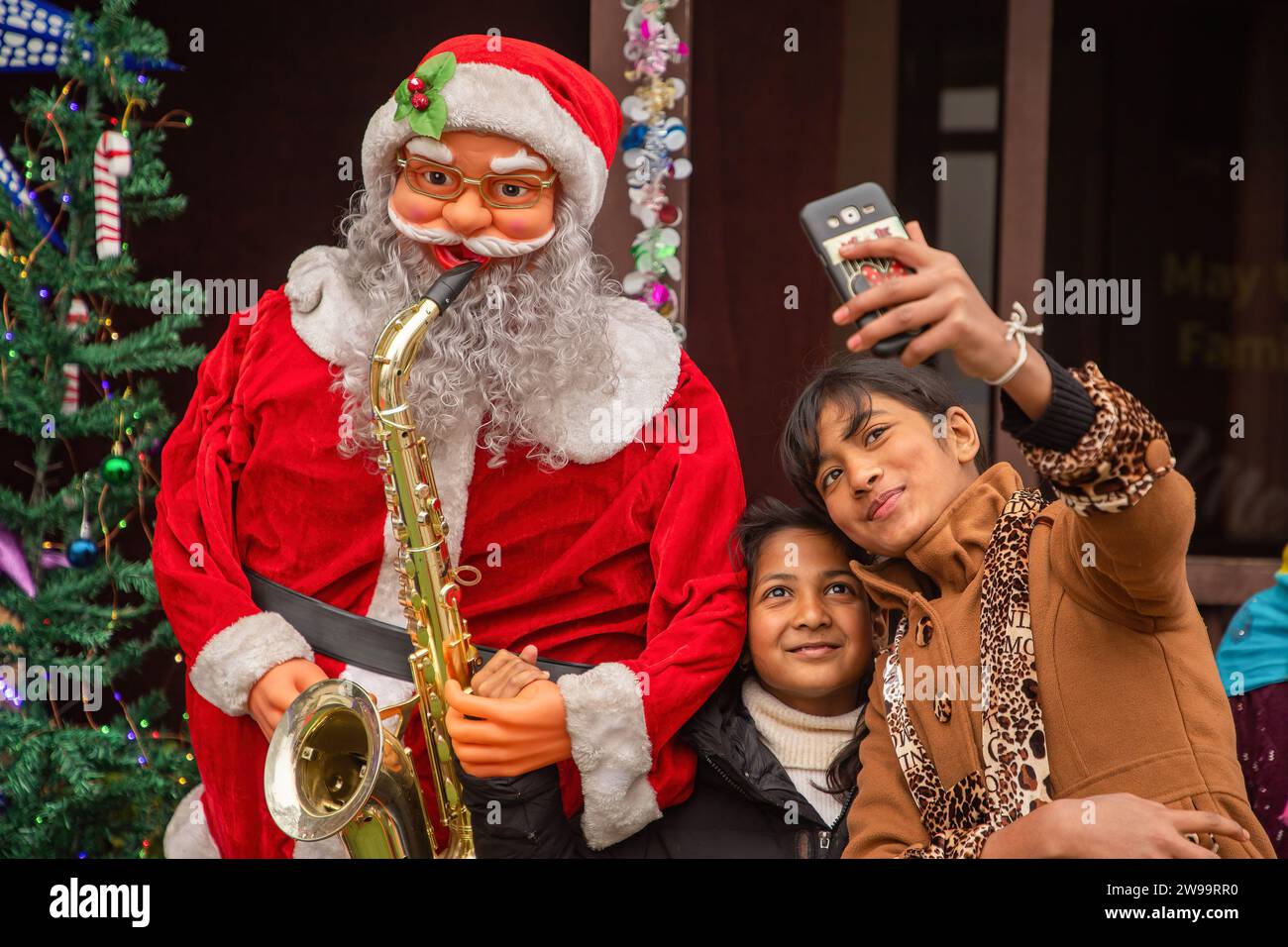 Srinagar, Inde. 25 décembre 2023. Des enfants chrétiens prennent un selfie avec le Père Noël devant l'église catholique de la Sainte famille un jour de Noël à Srinagar. La région himalayenne contestée du Cachemire a une minuscule population de chrétiens, dont des centaines se joignent à la messe à l'église catholique de la Sainte famille à Noël et prient pour la paix au Cachemire et en Palestine. Beaucoup viennent vêtus de costumes de Santa Clause pour célébrer Noël. Crédit : SOPA Images Limited/Alamy Live News Banque D'Images