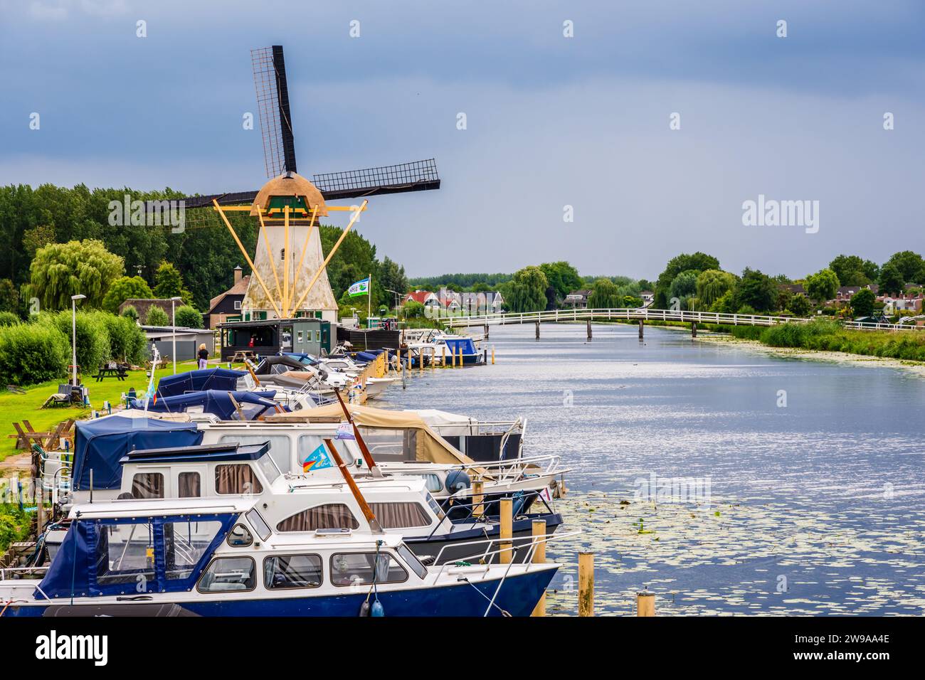 Le moulin à vent Kortlandse près de Rotterdam, aux pays-Bas, avec des bateaux fluviaux amarrés le long du canal et la passerelle Witte Brug par une journée d'été orageuse. Banque D'Images