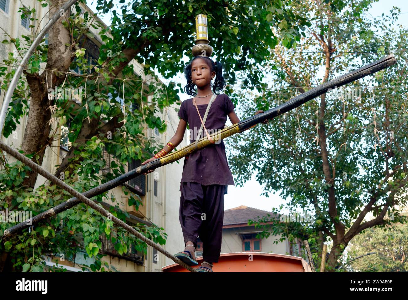 Dans un spectacle de rue ou tamasha, une jeune fille indienne marche sur une corde raide, avec la difficulté supplémentaire d'équilibrer des vaisseaux sur sa tête ; Mumbai, Inde Banque D'Images