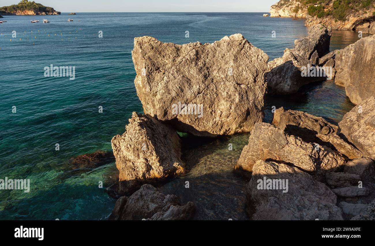 Calme mer verte claire au rivage avec de grands rochers, le soleil brille de petites vagues, paysage typique à l'une des nombreuses baies de Liapades, Grèce. Banque D'Images