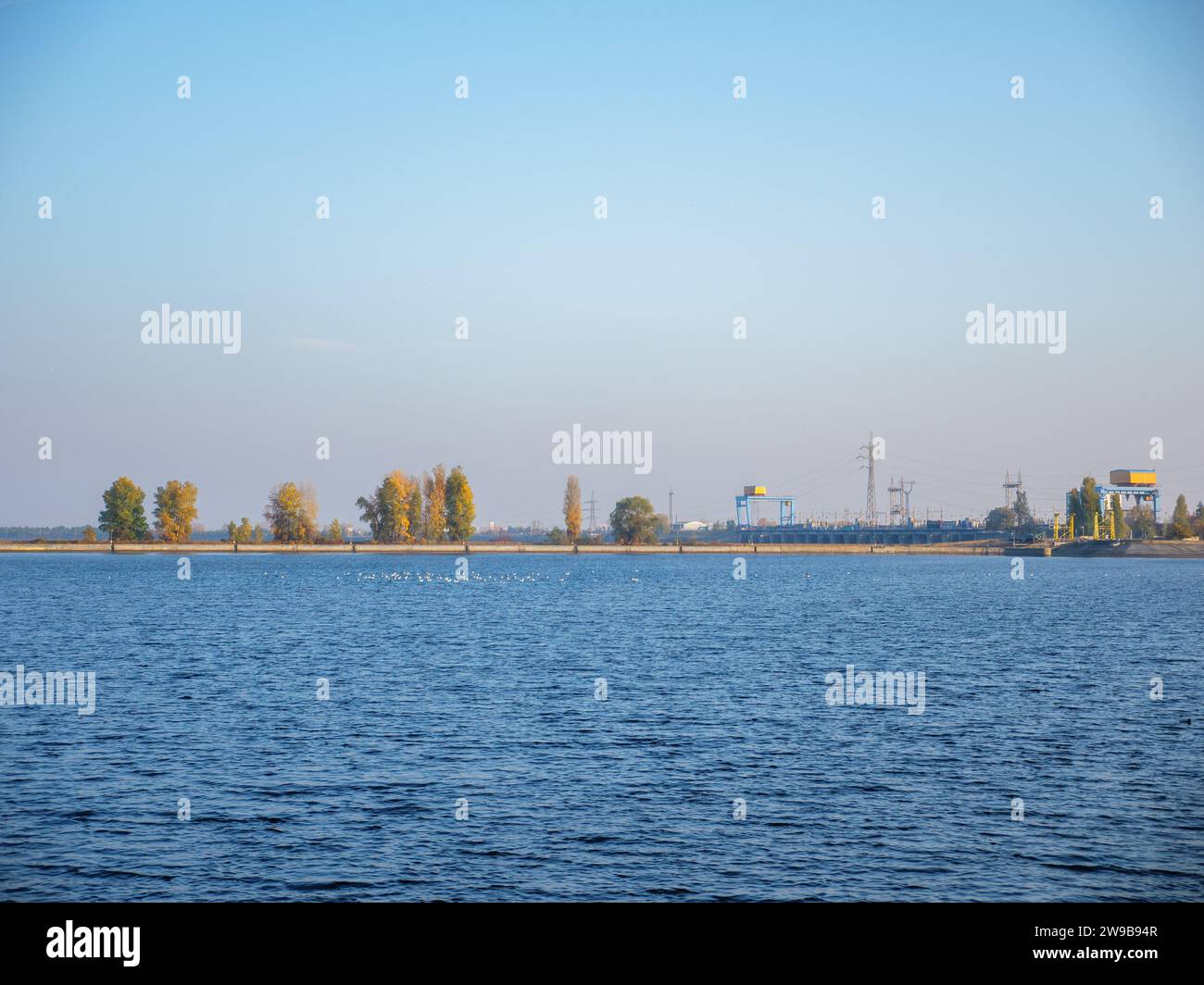 Un grand troupeau d'oiseaux volant au-dessus de la broche de la mer de Kiev, eau bleue calme avec yacht et bateau flottant, ciel bleu et rose, bande de rive étroite à l'horizon Banque D'Images