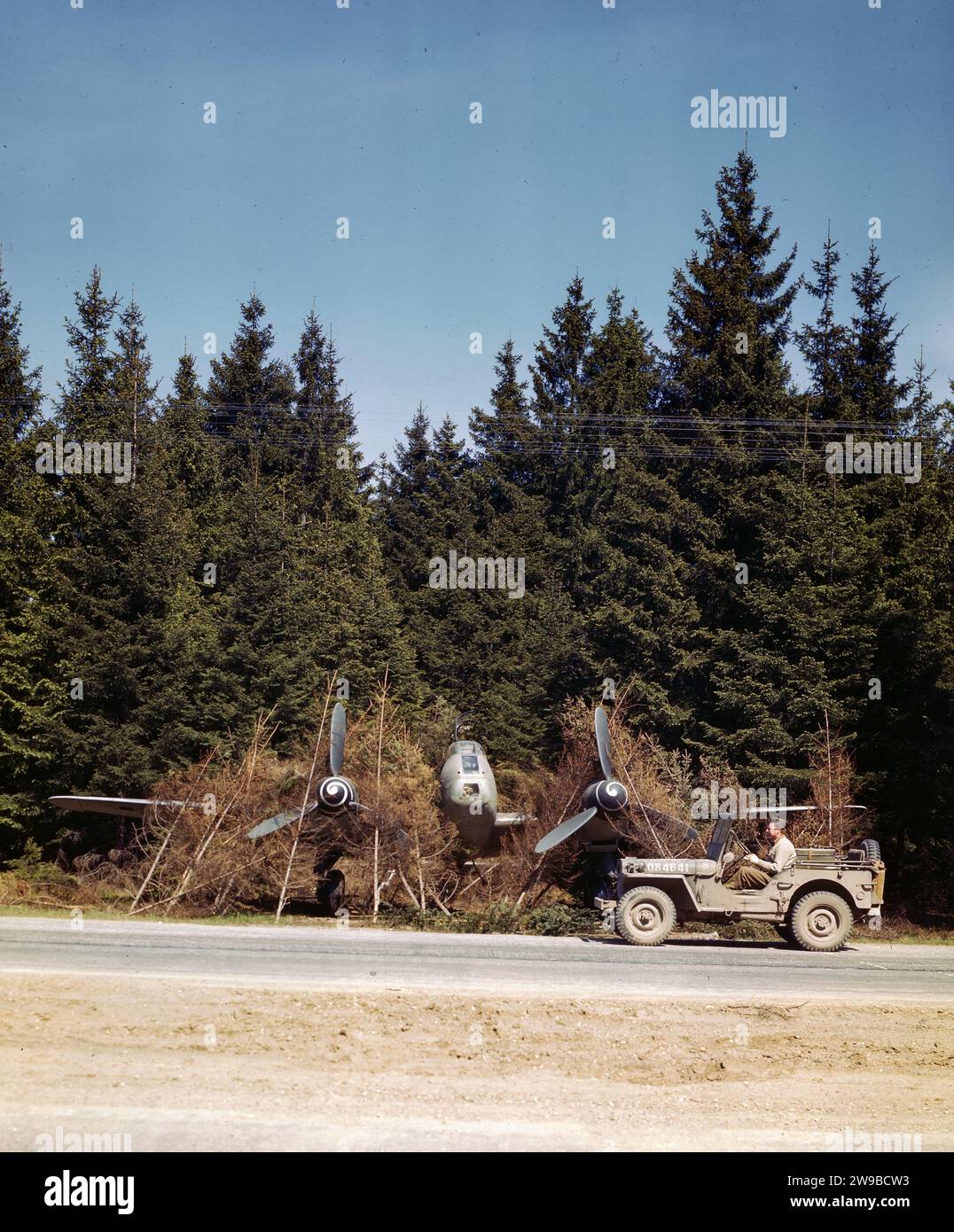 Un chasseur bombardier allemand camouflé stationné le long de l'Autobahn (super autoroute près de Munich) est inspecté par un GI dans une jeep. En raison des bombardements intensifs des aérodromes, les Allemands utilisèrent l'Autobahn comme piste 1945 Banque D'Images