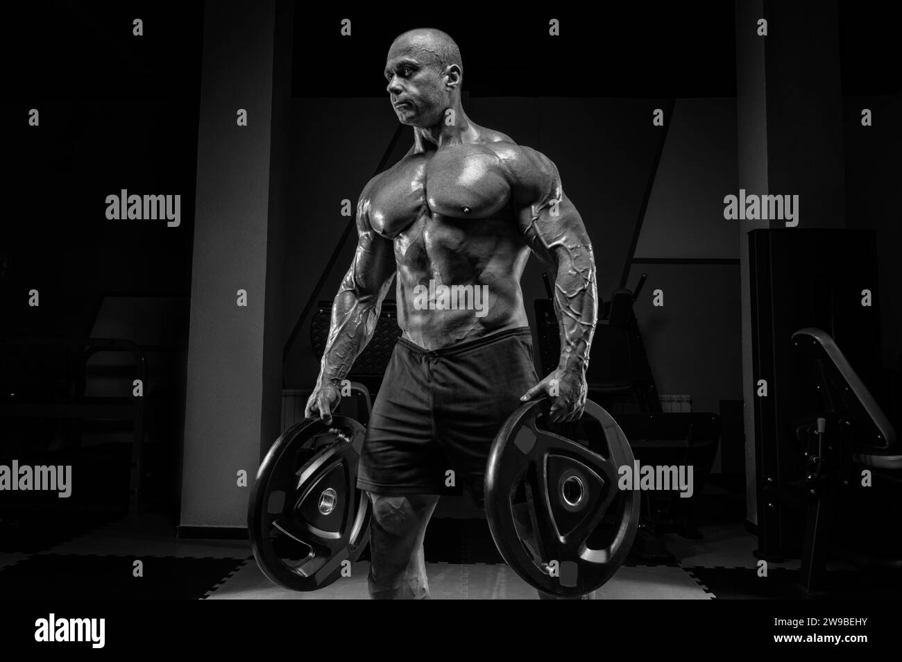 Homme musclé se tient dans une salle de gym avec des disques de barre. Concept de culturisme et de levage hydraulique. Supports mixtes Banque D'Images
