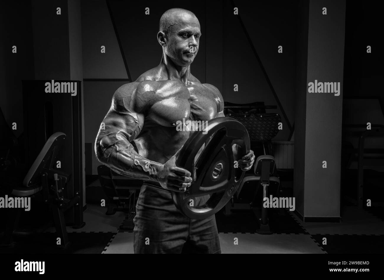 Homme musclé posant dans la salle de gym avec un disque de barre. Concept de culturisme et de levage hydraulique. Supports mixtes Banque D'Images