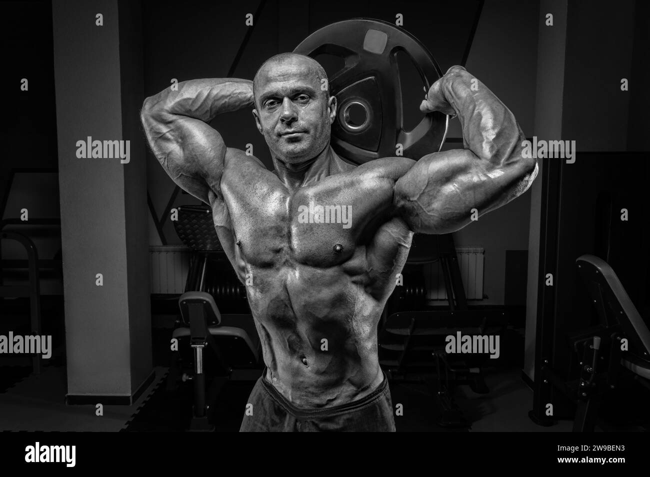 Homme musclé posant dans la salle de gym avec un disque de barre. Concept de culturisme et de levage hydraulique. Supports mixtes Banque D'Images