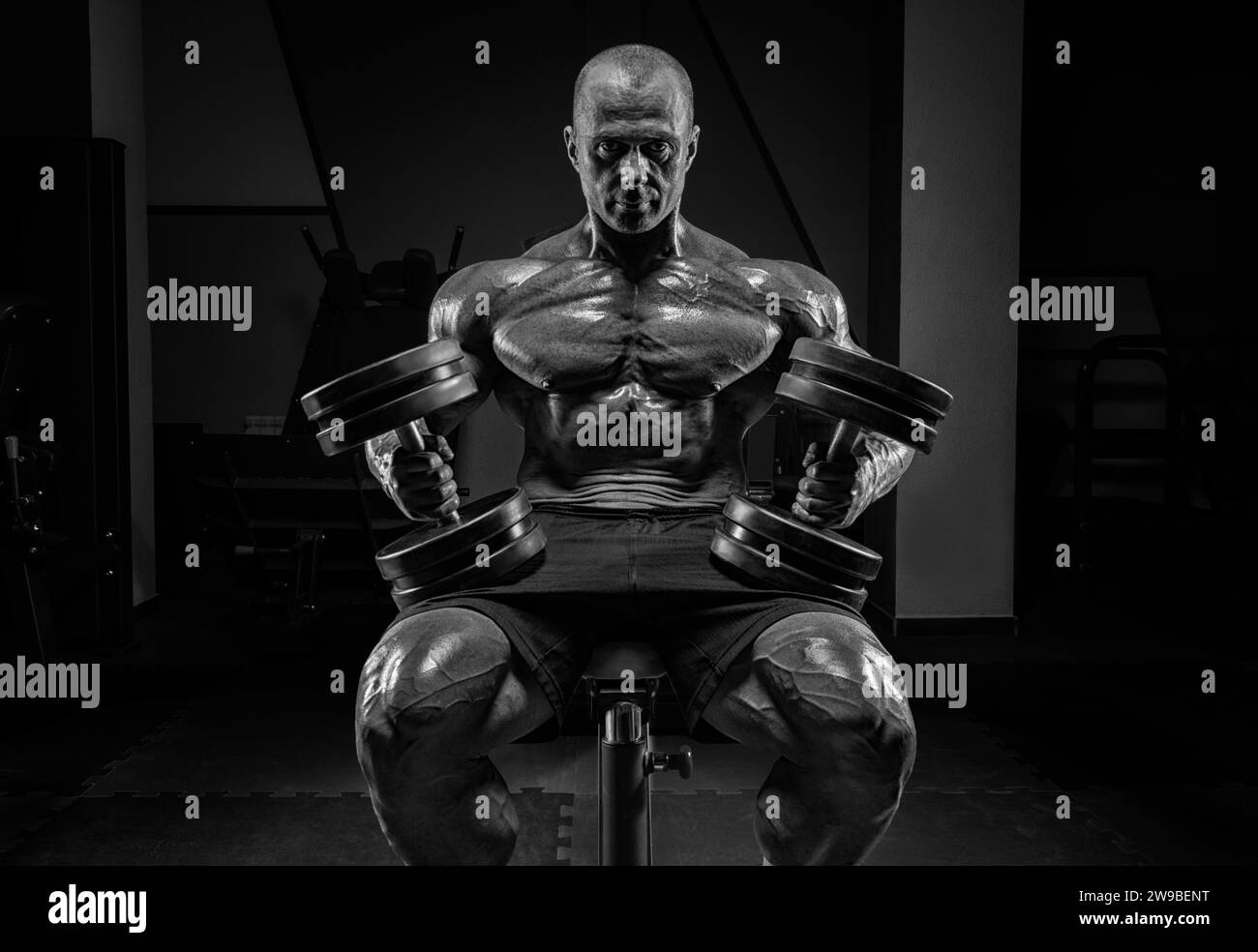 Homme musclé assis sur un banc avec des haltères. Concept de culturisme et de levage hydraulique. Supports mixtes Banque D'Images
