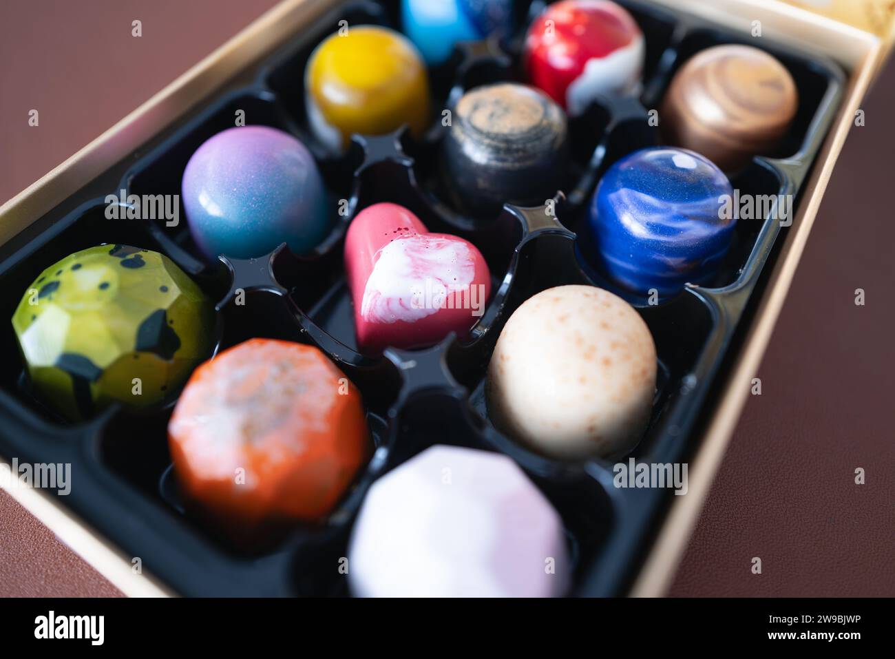 Un chocolat en forme de foyer dans une boîte de friandises artisanales colorées fabriquées à la main dans une boîte de présentation. Ils ont des coquilles lisses avec de jolis motifs. Banque D'Images