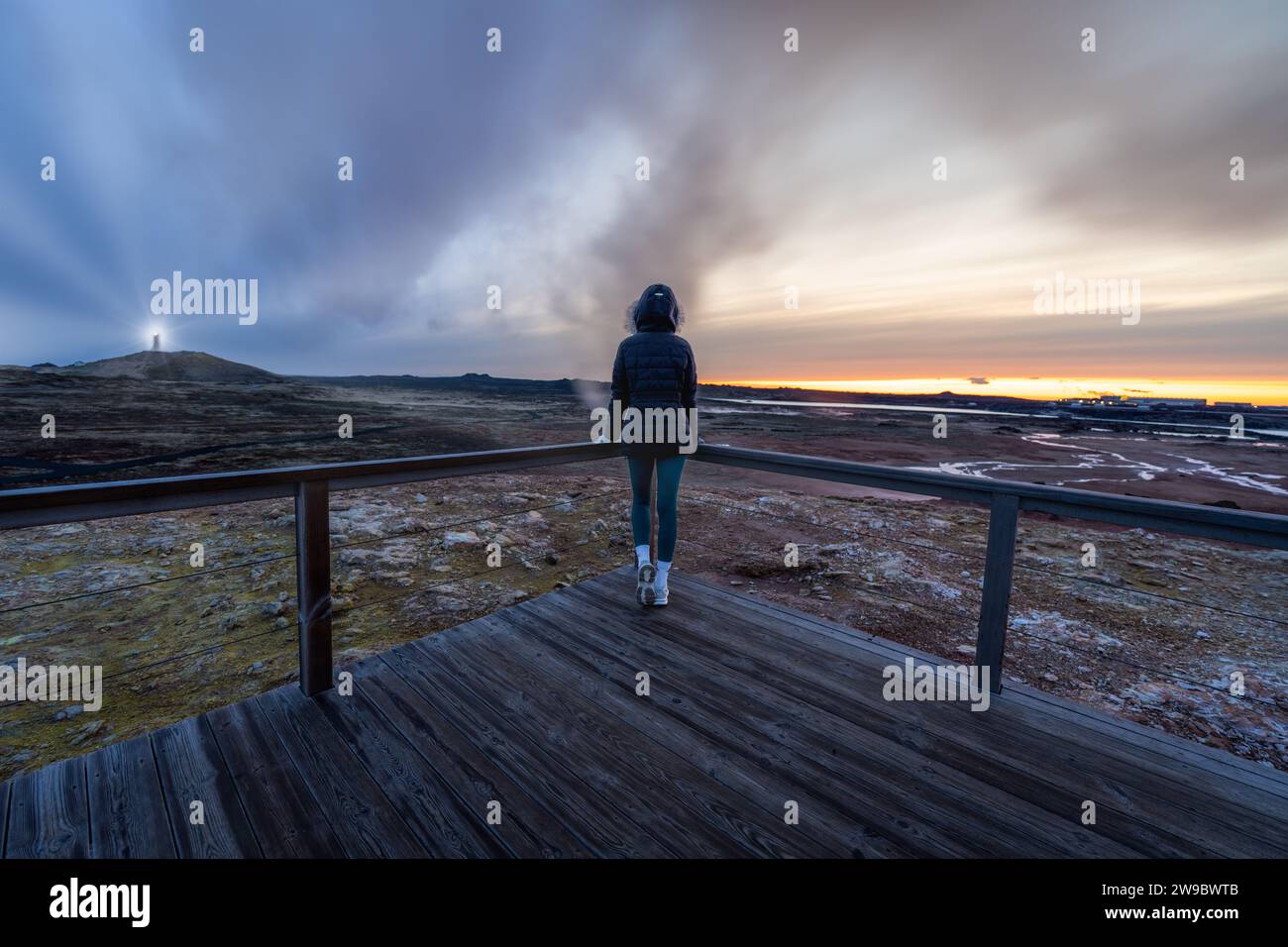 Femme posant devant un phare et des terres enfumées en Islande Banque D'Images