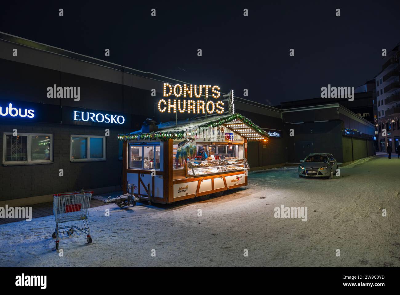 Vue rapprochée d'un kiosque de rue vendant des beignets et des churros illuminés sur une soirée d'hiver. Banque D'Images