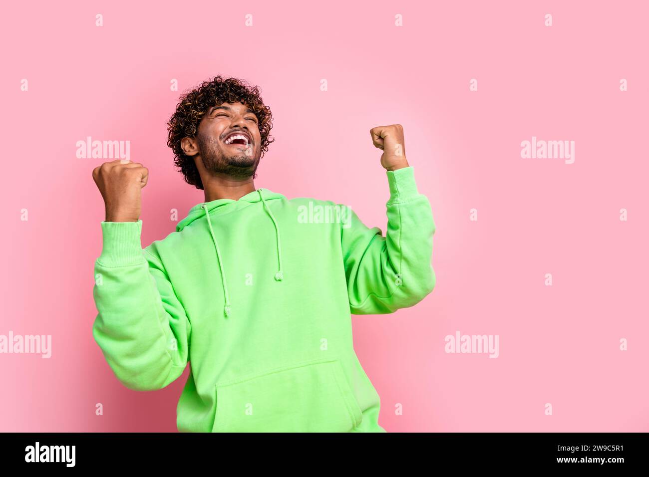 Photo de gars fou dans le pull tendance vert Profitez des vêtements de sortie de marque adidas à vendre poings levés vers le haut isolé sur fond de couleur rose Banque D'Images