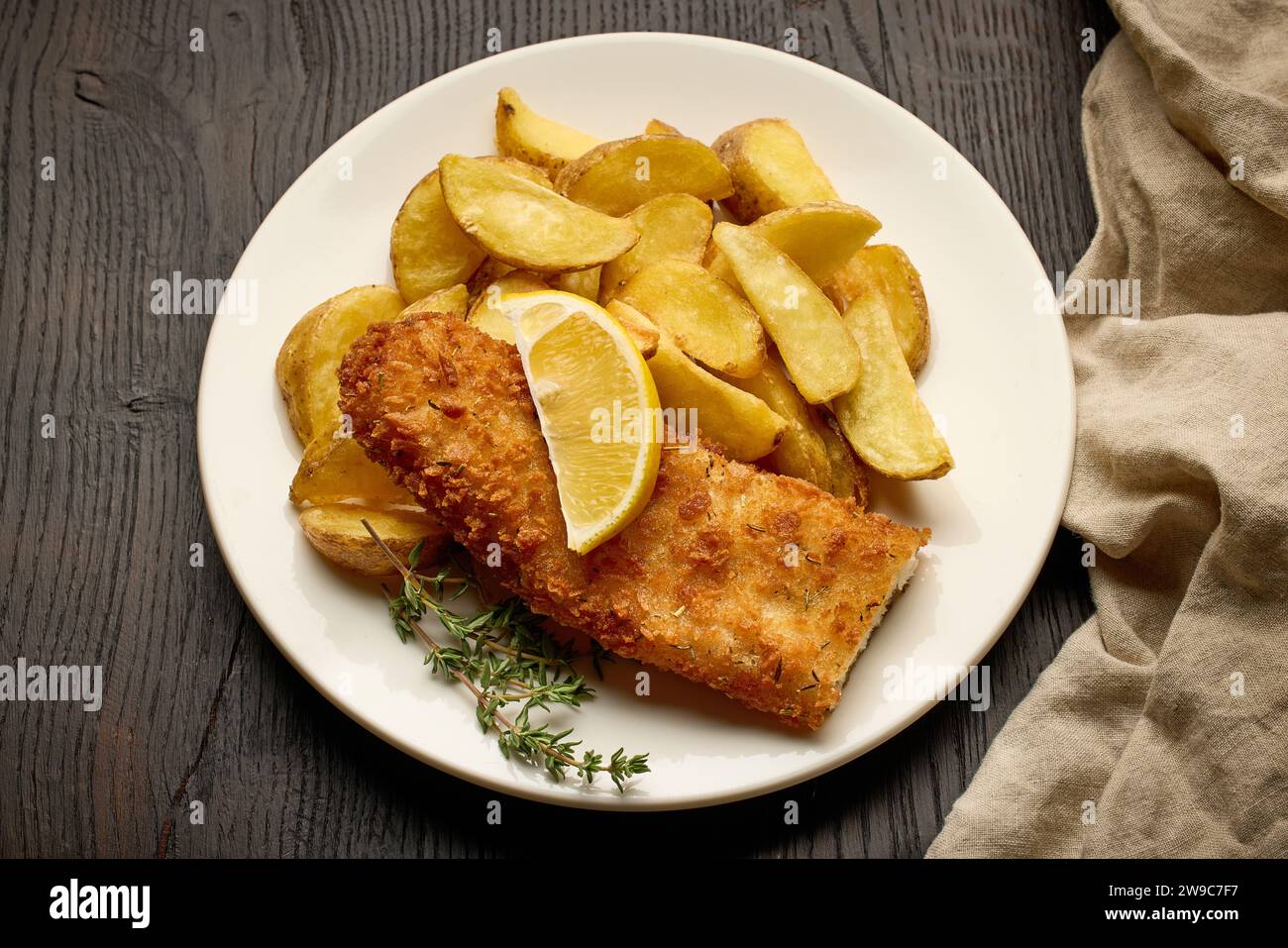 assiette de fish and chips, filet de poisson pané et quartiers de pommes de terre frites sur une table en bois foncé, vue de dessus Banque D'Images