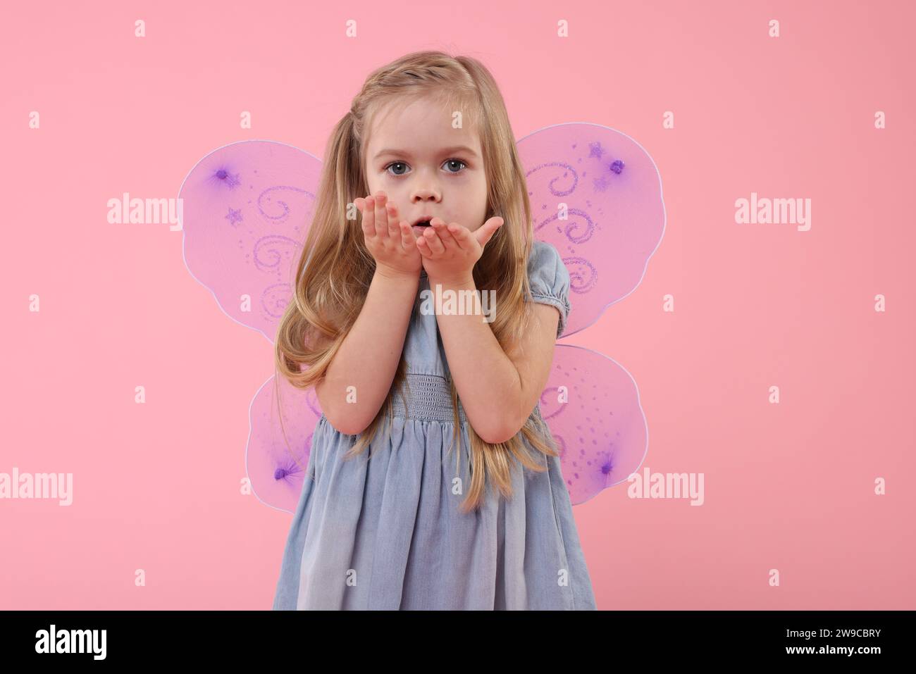 Mignonne petite fille en costume de fée avec des ailes violettes soufflant baiser sur fond rose Banque D'Images