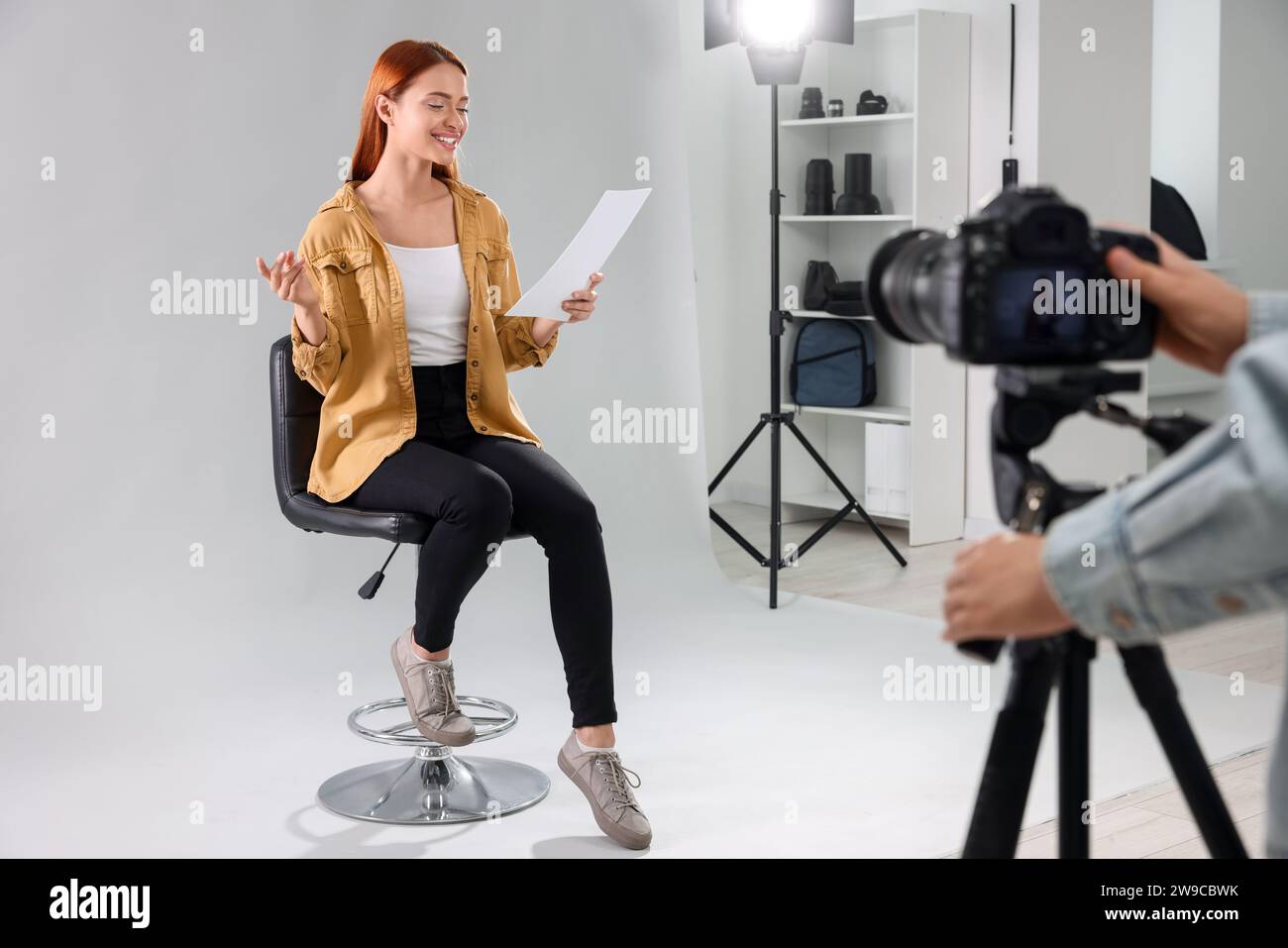 Appel de casting. Femme avec script jouant pendant que le caméraman la filme sur fond gris clair en studio Banque D'Images