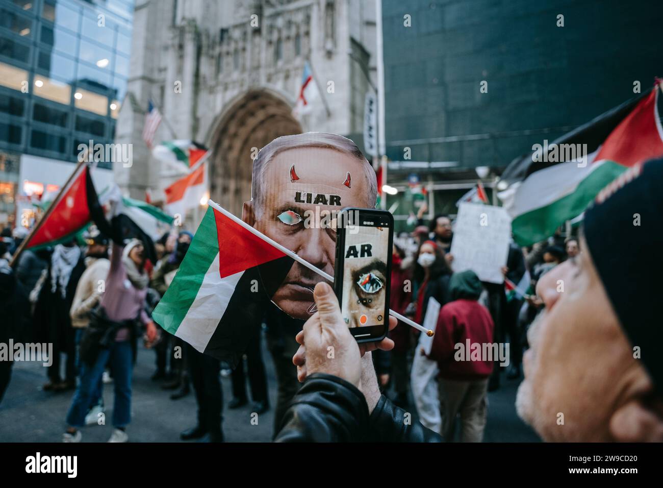 Un manifestant pro-palestinien prend une photo de l'un des manifestants portant un masque représentant le Premier ministre israélien Netanyahu pendant la manifestation. Le jour de Noël, après avoir construit une scène de nativité avec des décombres, du faux sang et des poupées inusées, des centaines de partisans de la Palestine à New York descendent dans la rue pour appeler à un cessez-le-feu immédiat à Gaza. La manifestation est organisée en solidarité avec les églises chrétiennes de Bethléem, qui ont annulé les célébrations de Noël en raison du bombardement continu de Gaza. (Photo Olga Fedorova/SOPA Images/Sipa USA) Banque D'Images