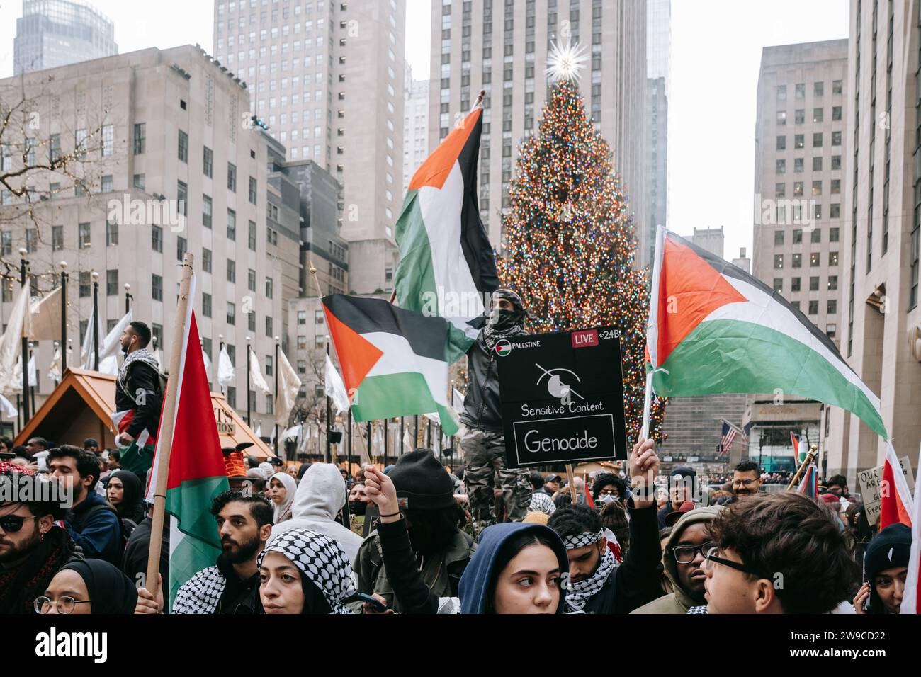 Les manifestants brandissent des drapeaux palestiniens, au Rockefeller Center, devant le plus grand sapin de Noël des États-Unis pendant la manifestation. Le jour de Noël, après avoir construit une scène de nativité avec des décombres, du faux sang et des poupées inusées, des centaines de partisans de la Palestine à New York descendent dans la rue pour appeler à un cessez-le-feu immédiat à Gaza. La manifestation est organisée en solidarité avec les églises chrétiennes de Bethléem, qui ont annulé les célébrations de Noël en raison du bombardement continu de Gaza. (Photo Olga Fedorova/SOPA Images/Sipa USA) Banque D'Images