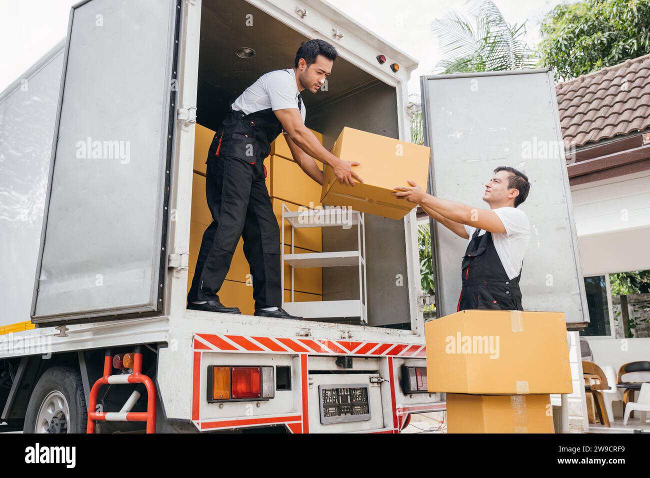 Les travailleurs en uniforme font preuve d'un travail d'équipe en déchargeant les boîtes en carton du camion de déménagement pour le client Banque D'Images