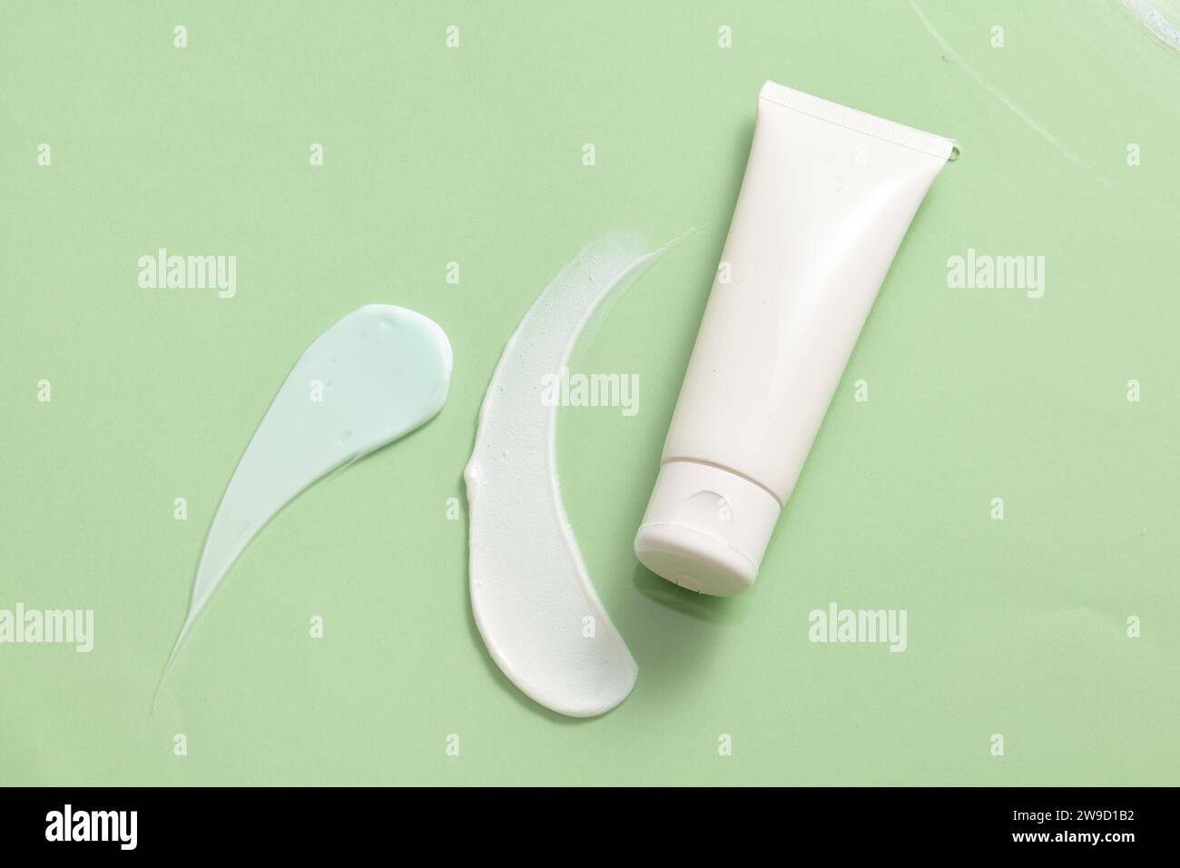 Tube cosmétique blanc et non marqué orné de stries de cosmétiques sur fond vert clair. Tache cosmétique sur fond clair gros plan. Sk naturel Banque D'Images