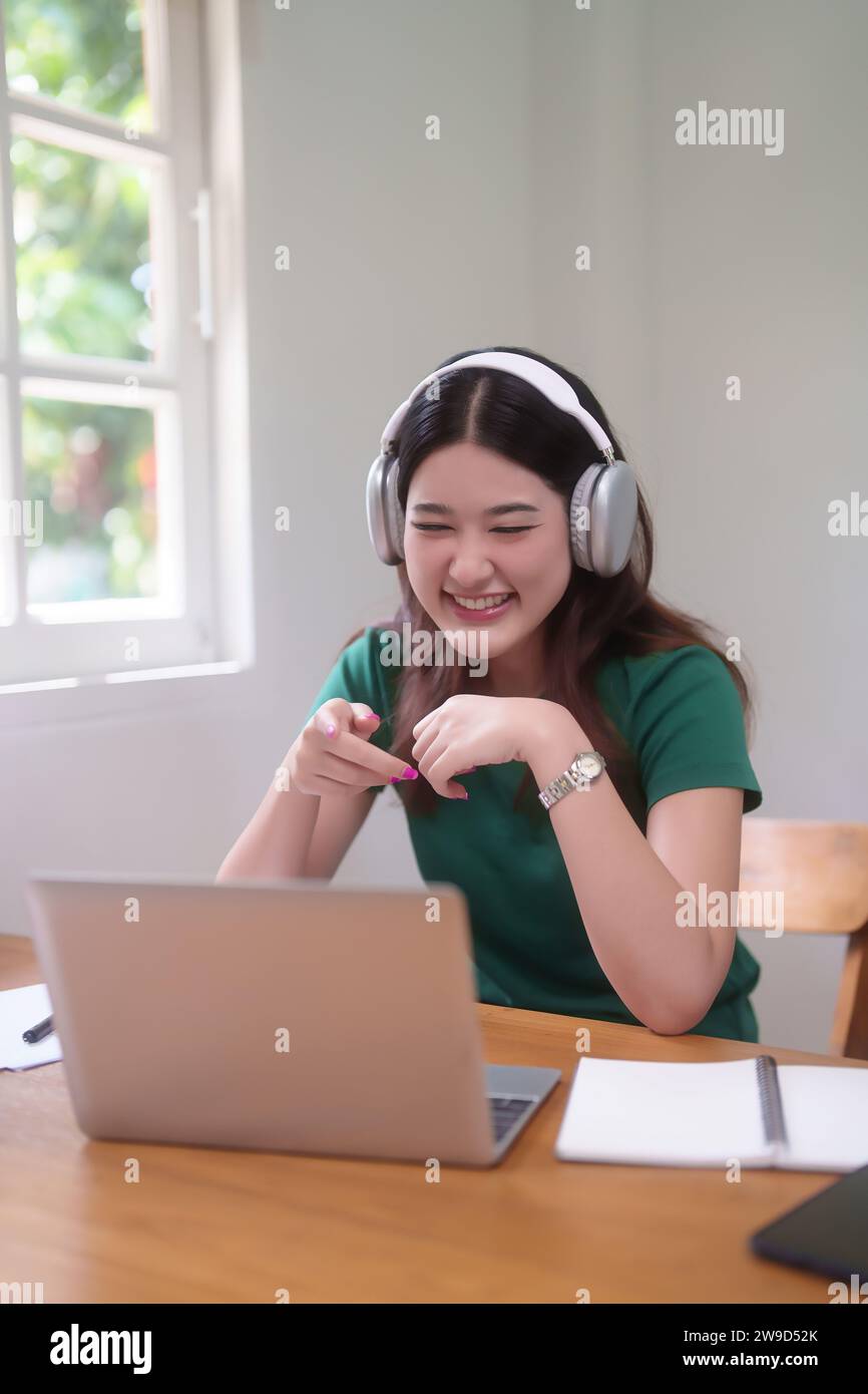 Les jeunes étudiantes asiatiques portent des écouteurs et de la communication par le biais de chat vidéo en classe en ligne sur ordinateur portable tout en étudiant et en regardant le webinaire de conférence à Banque D'Images