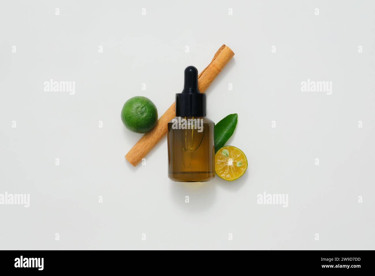 Un flacon compte-gouttes ambré décoré avec des ingrédients pour les huiles essentielles naturelles sur fond blanc. Le citron, le kumquat et la cannelle sont tous des huiles essentielles Banque D'Images