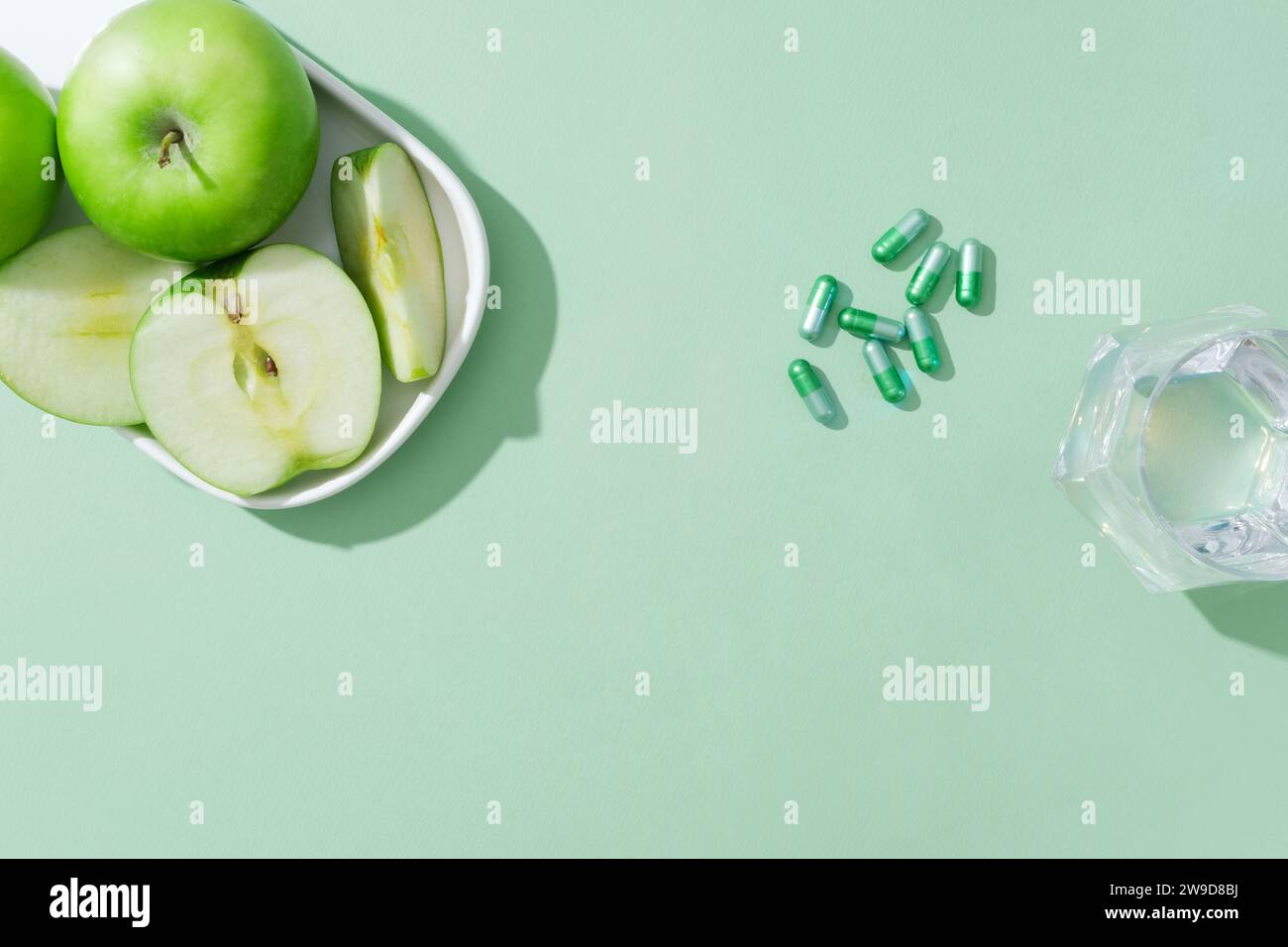 Sur le fond vert, des plats de pommes vertes avec des pilules de capsule et une tasse en verre décorée. Espace vide pour le produit de présentation, le poids de support Banque D'Images