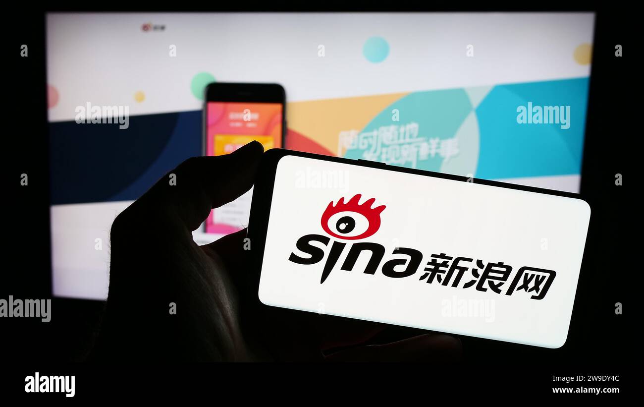 Personne tenant le smartphone avec le logo de la société de technologie chinoise Sina Corporation en face du site Web. Concentrez-vous sur l'affichage du téléphone. Banque D'Images