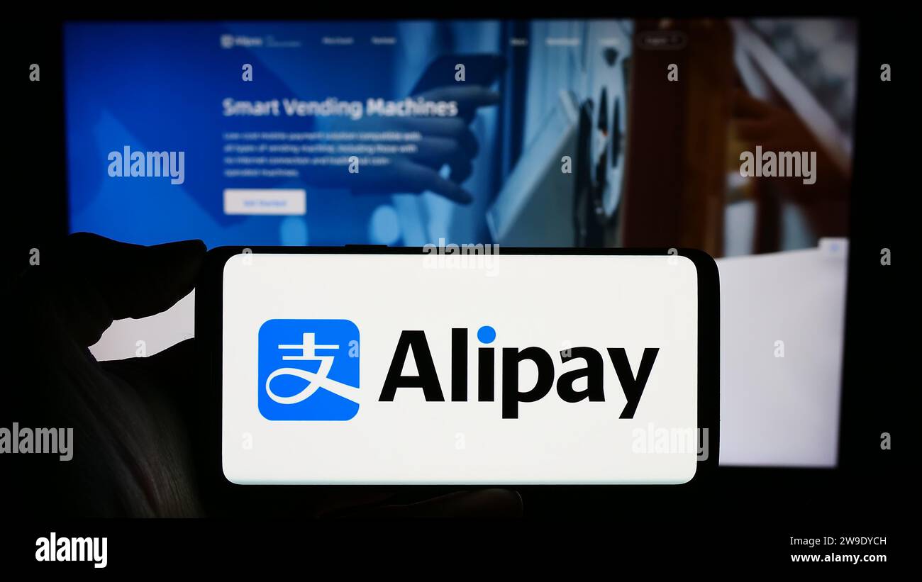 Personne tenant le téléphone portable avec le logo de la société chinoise de plate-forme de paiement Alipay en face de la page Web d'affaires. Concentrez-vous sur l'affichage du téléphone. Banque D'Images