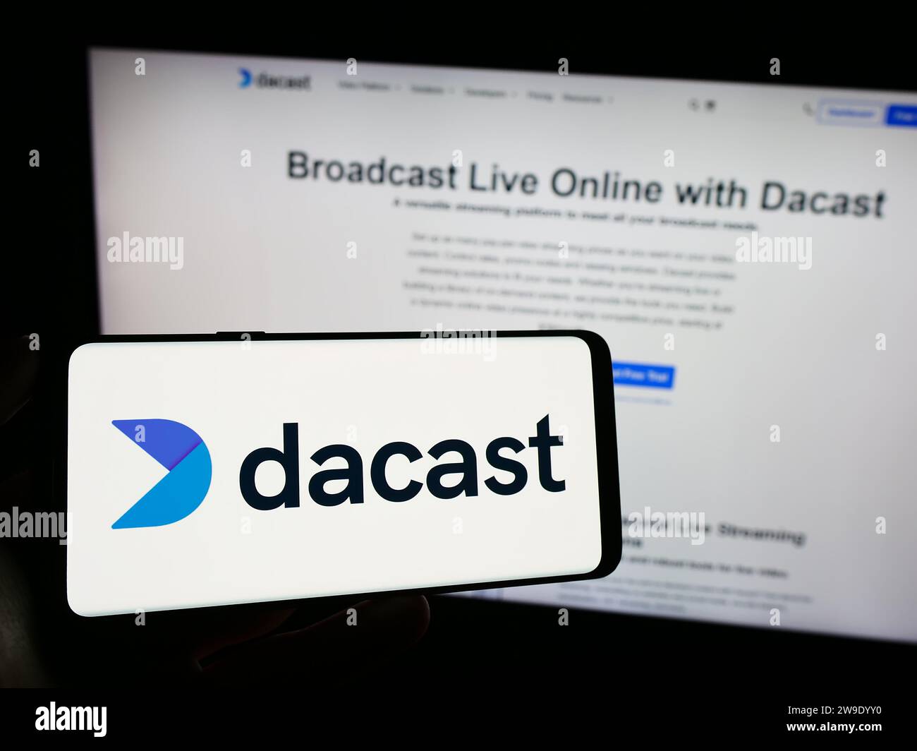 Personne détenant un téléphone cellulaire avec le logo de la société de streaming vidéo en direct Dacast Inc. Devant la page Web de l'entreprise. Concentrez-vous sur l'affichage du téléphone. Banque D'Images