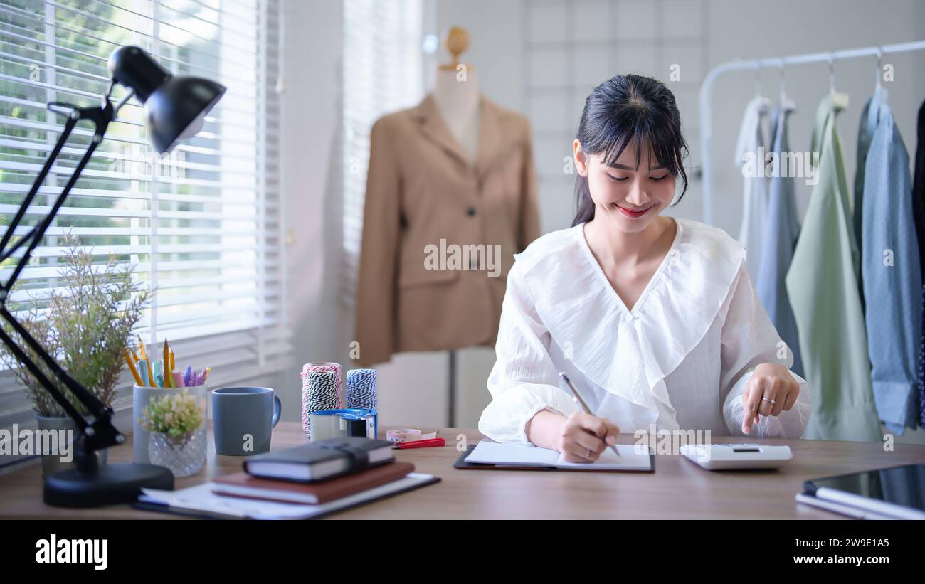 Jeunes femmes marchandes asiatiques utilisant la calculatrice pour calculer sur les finances des affaires d'achat en ligne et écrire des informations dans le cahier tout en travaillant Banque D'Images
