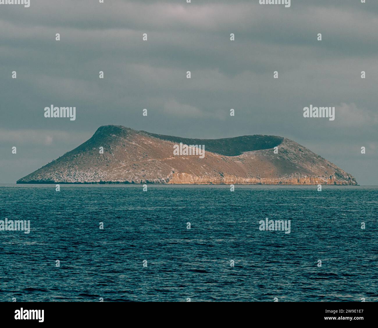 Île isolée dans les Galapagos, Équateur, entourée par les eaux bleues claires de l'océan Pacifique sous un ciel nuageux. Banque D'Images