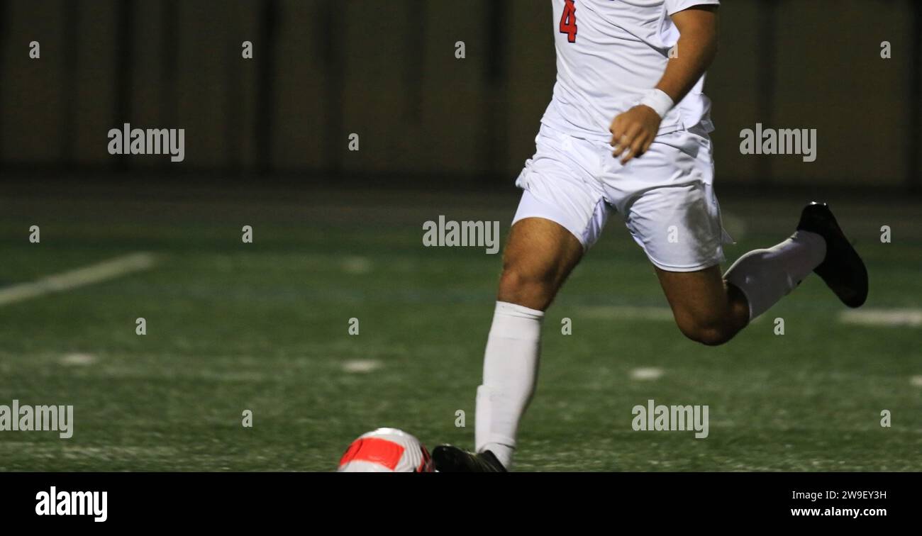 Un homme qui frappe un ballon de football sur un terrain la nuit sous les lumières. Banque D'Images