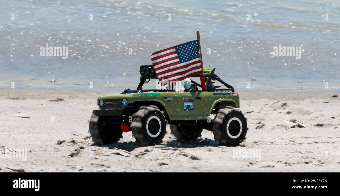 Un camion jouet vert avec un drapeau américain au-dessus de lui se déplaçant sur le sable à la plage. Banque D'Images