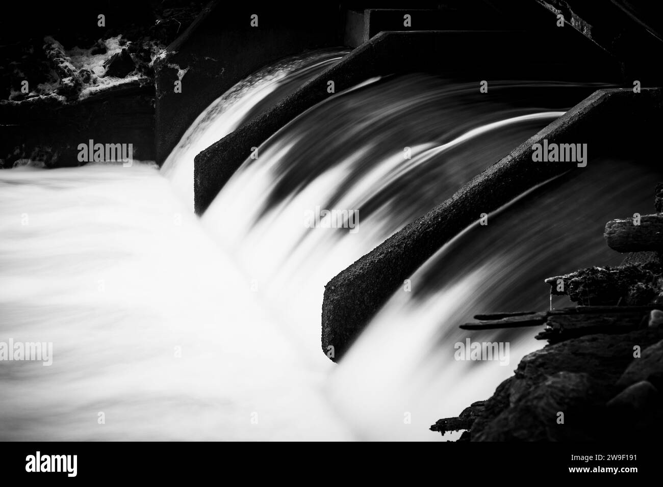 L'eau coule sur une structure de barrage et s'écrase au fond du déversoir créant de la mousse et laissant des sentiers sur l'eau au fond. Banque D'Images