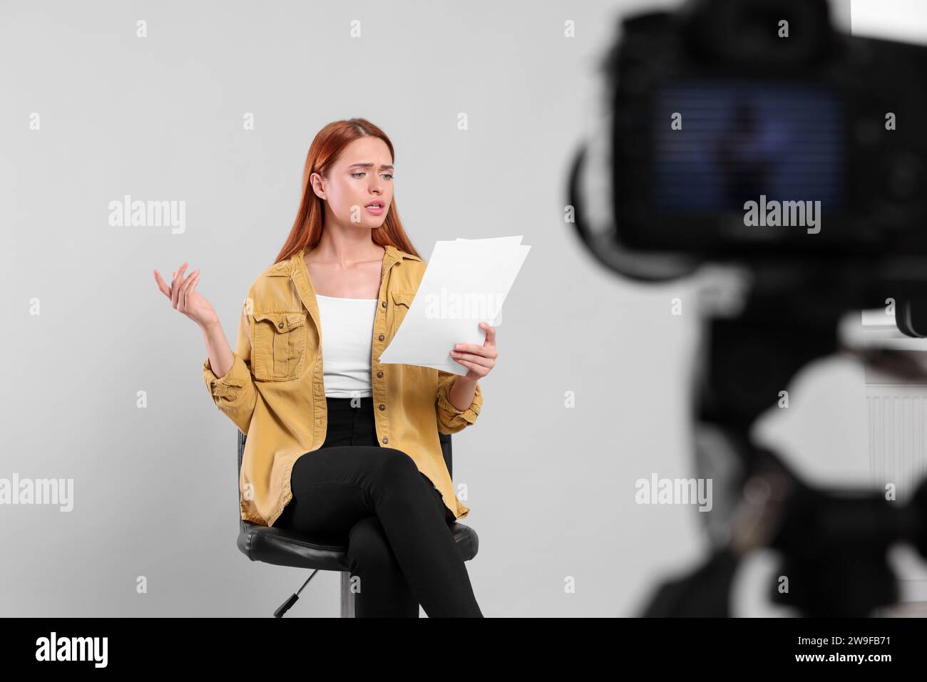 Appel de casting. Jeune femme avec script jouant devant la caméra sur fond gris clair au studio Banque D'Images