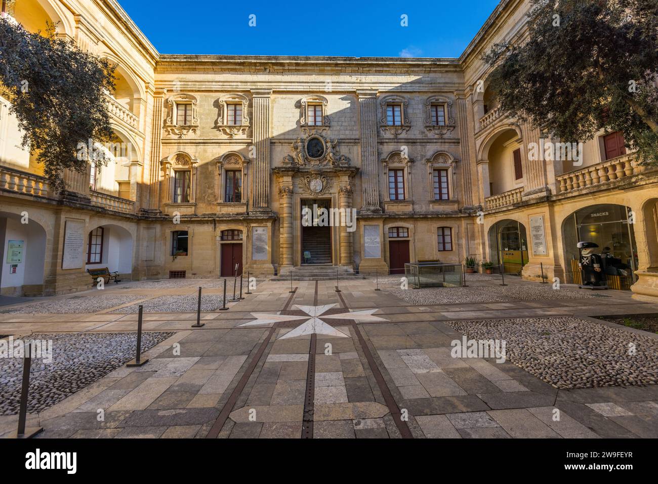 La cour du Palazzo Vilhena à Mdina présente une croix maltaise à huit pointes intégrée dans le pavage. Le Grand Maître António Manoel de Vilhena fit construire le palais en 1726–1728 par l'architecte français Charles François de Mondion dans le style baroque français. Cette cour figura parmi les lieux utilisés à Mdina pour la première saison de Game of Thrones en 2011. Banque D'Images