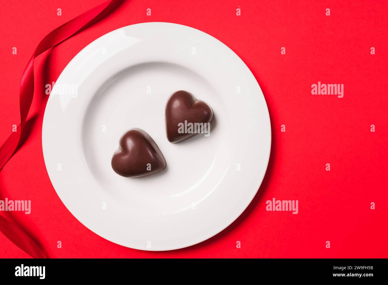 Deux bonbons au chocolat en forme de coeur sur l'assiette sur fond rouge, gâteries de Saint-Valentin Banque D'Images