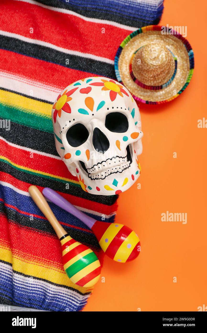 Crâne humain peint pour le jour des morts du Mexique (El Dia de Muertos) avec poncho, maracas et sombrero sur fond orange Banque D'Images