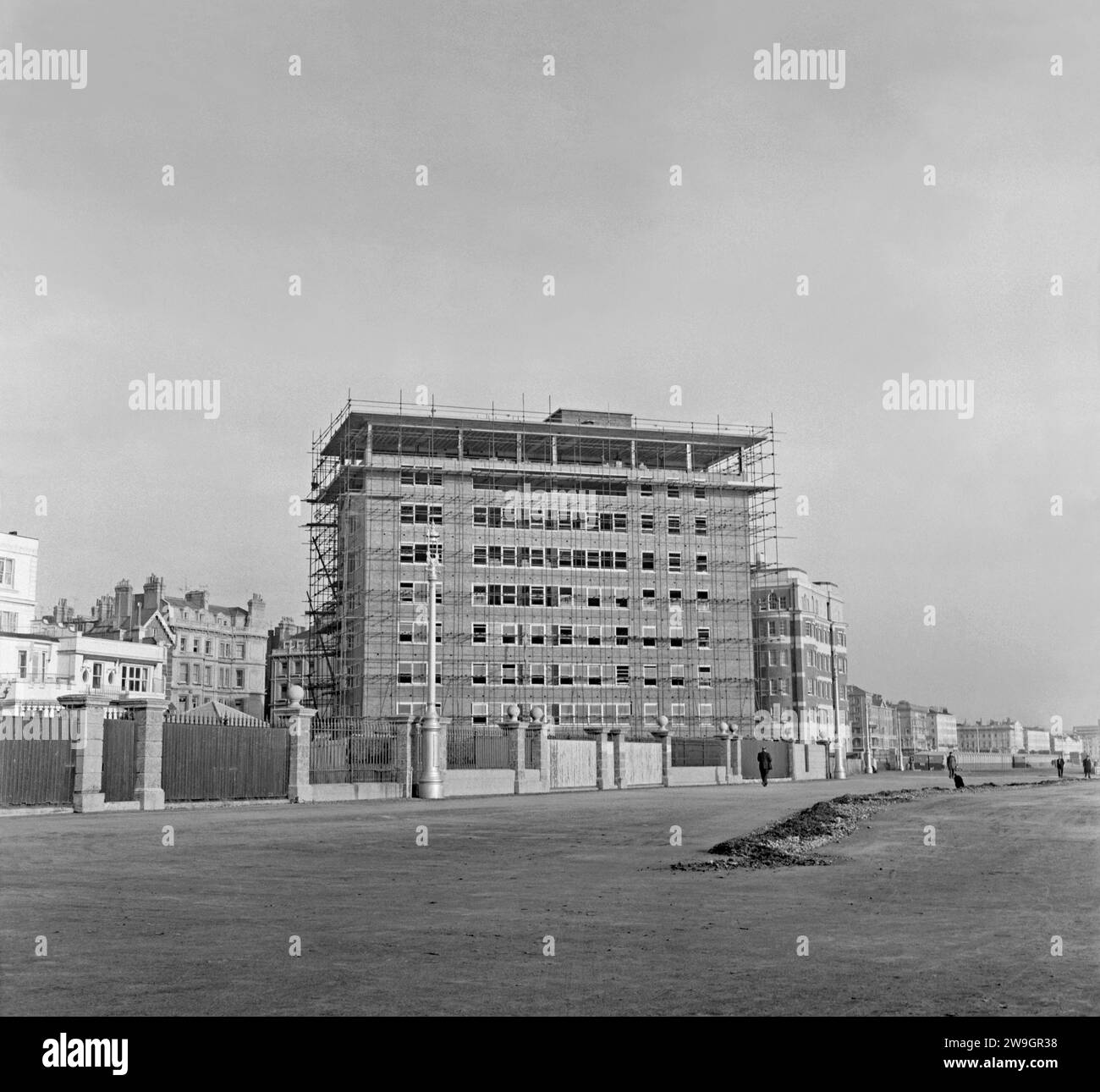 Une vue vers l'est le long de la promenade du front de mer à King's Esplanade, Hove, Brighton et Hove, East Sussex, Angleterre, Royaume-Uni c. 1958. Le développement moderne a lieu avec Flag court en construction - le bloc de luxe de 54 appartements a été achevé en 1959. Il est incliné de sorte que la plupart des appartements ont une vue sur la mer. Derrière ce bloc se trouve le plus ancien bloc de 1934, Courtenay Gate sur Courtenay Terrace, Kingsway. Les jardins arrière des vieilles maisons de Courtenay Terrace sont visibles sur la gauche. Le conseil municipal de Hove s'est approprié une partie de leurs jardins pour agrandir le promenad - une photographie vintage des années 1950. Banque D'Images