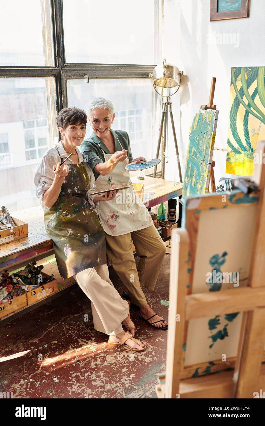 artistes féminins matures souriants pointant vers le chevalet avec atelier d'artisanat de pinceau, passe-temps créatif Banque D'Images