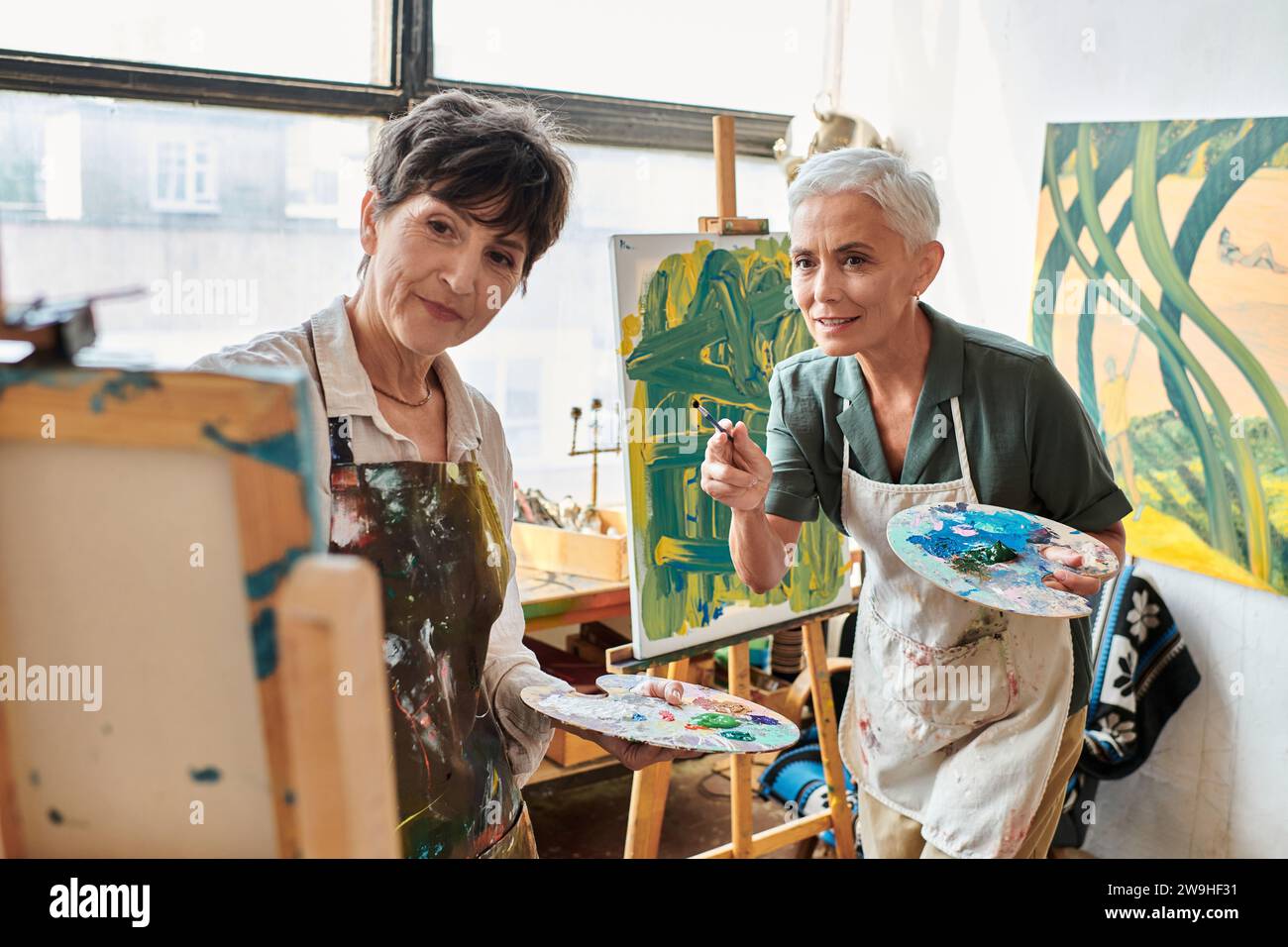 artistes femmes matures avec palettes regardant le chevalet dans l'atelier d'art, la créativité et la collaboration Banque D'Images