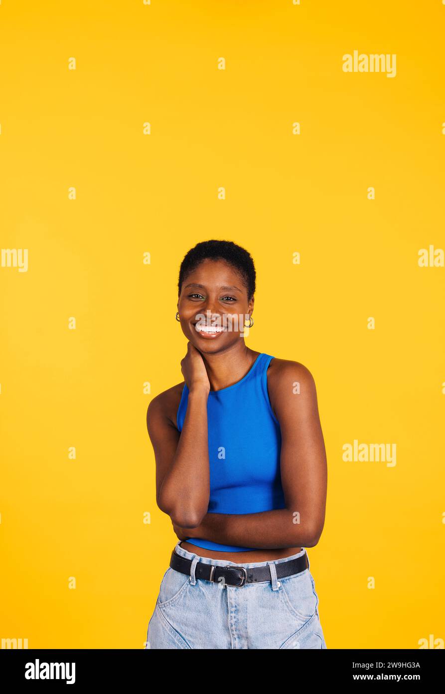 Portrait d'une jeune belle femme joyeuse portant des vêtements bleus debout sur un fond jaune. Jeune femme regardant la caméra. Banque D'Images