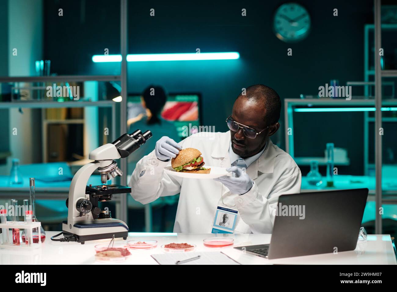 Scientifique afro-américain examinant un hamburger avec de la viande cultivée en laboratoire assis sur son lieu de travail en laboratoire Banque D'Images Scientifique afro-américain examinant un hamburger avec de la viande cultivée en laboratoire assis sur son lieu de travail en laboratoire Banque D'Images