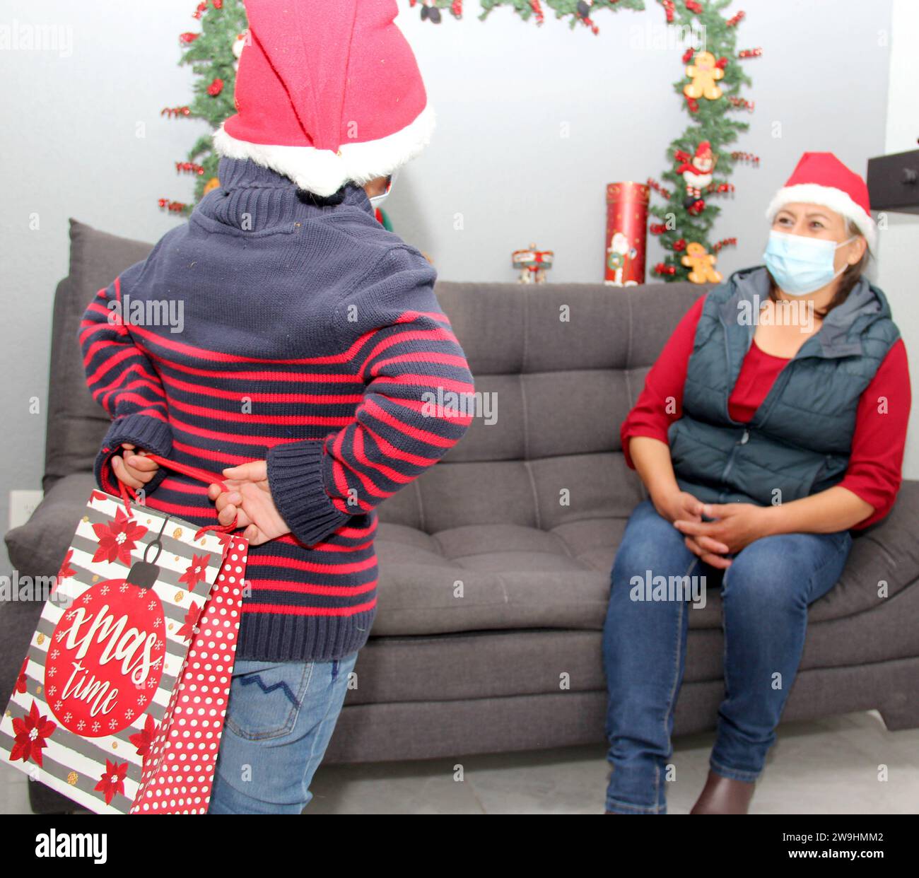 Grand-mère et enfant avec masque de protection et chapeau du père noël, cadeaux et décorations de Noël, nouveau covid-19 normal Banque D'Images