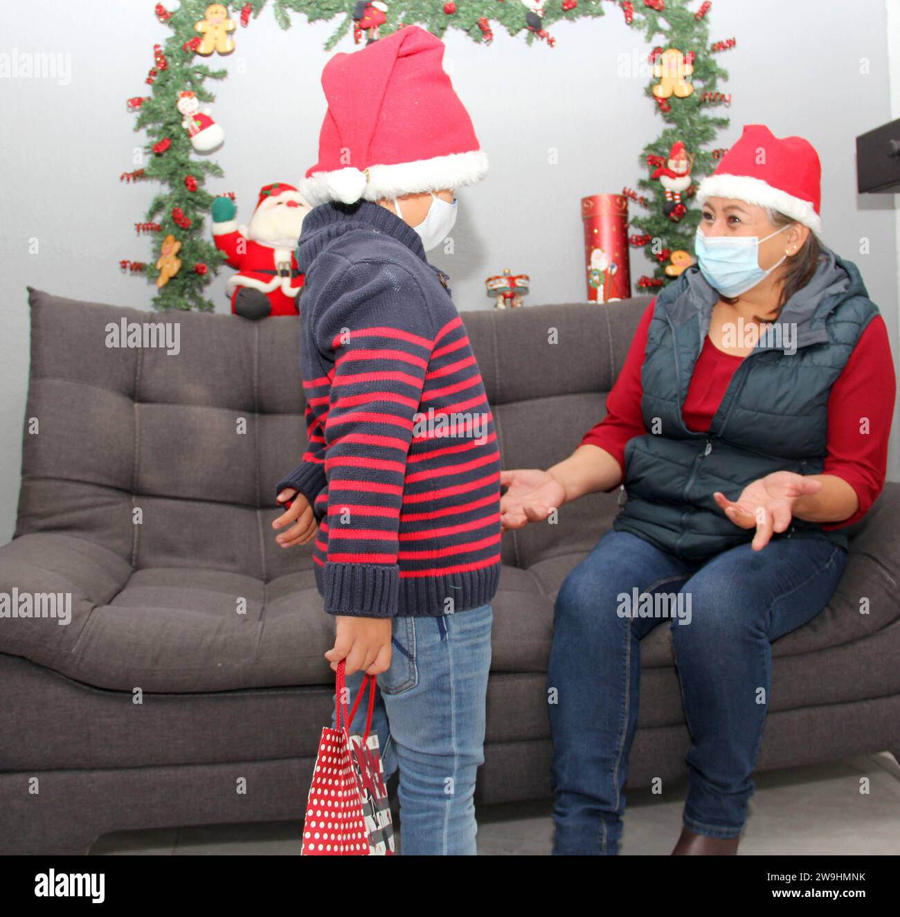 Grand-mère et enfant avec masque de protection et chapeau du père noël, cadeaux et décorations de Noël, nouveau covid-19 normal Banque D'Images