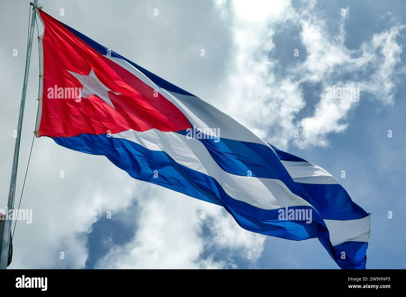 Drapeau de Cuba hissant fièrement dans l'air sur un jour lumineux avec ciel bleu et nuages. Banque D'Images