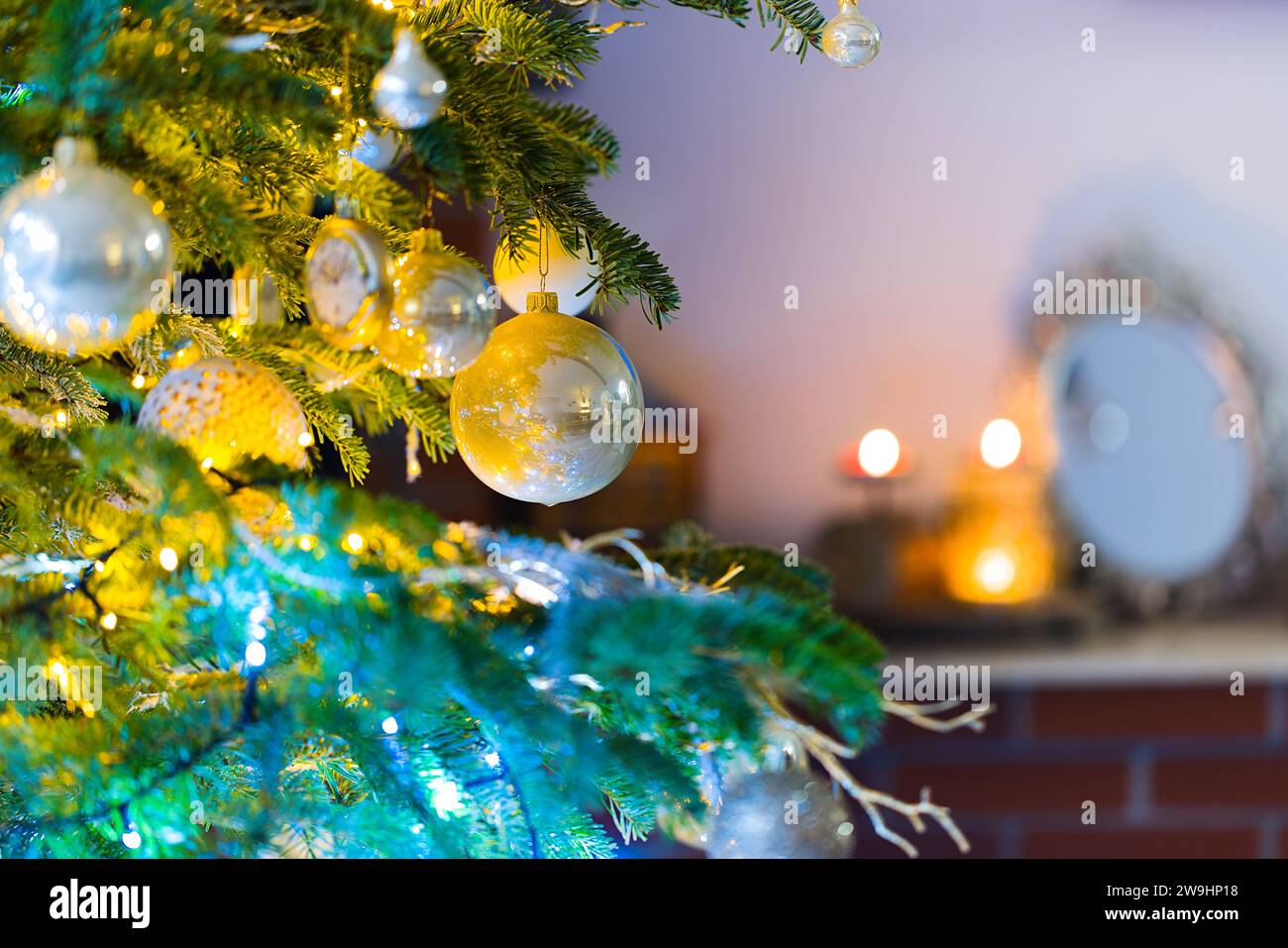 Des ornements suspendus illuminent un sapin de Noël, entouré par la lueur douce des lumières de Noël floues. Banque D'Images